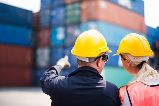 Zwei Hafenarbeiter mit Helmen vor Containern, Logistik und Transportplanung